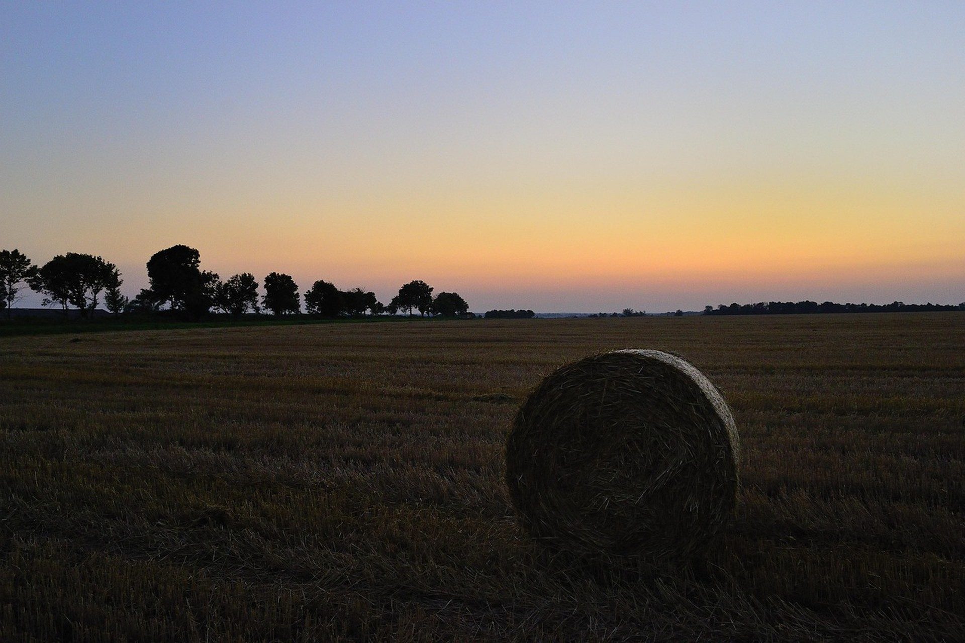 Una sola paca redonda de heno en un campo cosechado oscuro bajo un cielo de atardecer naranja y púrpura